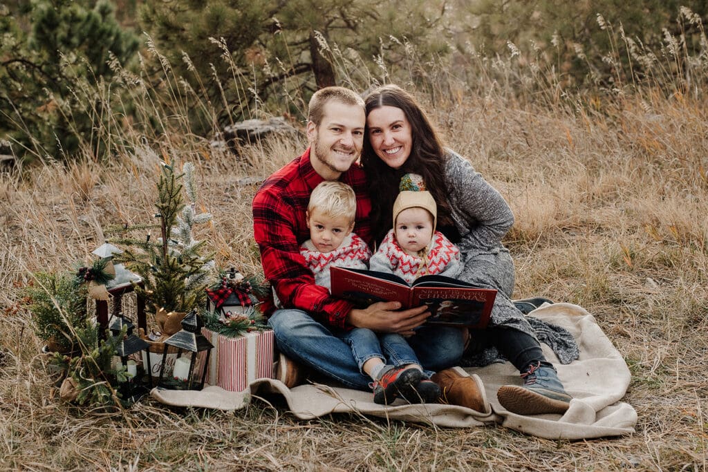 Family reading a Christmas book sitting in a field with Christmas decorations