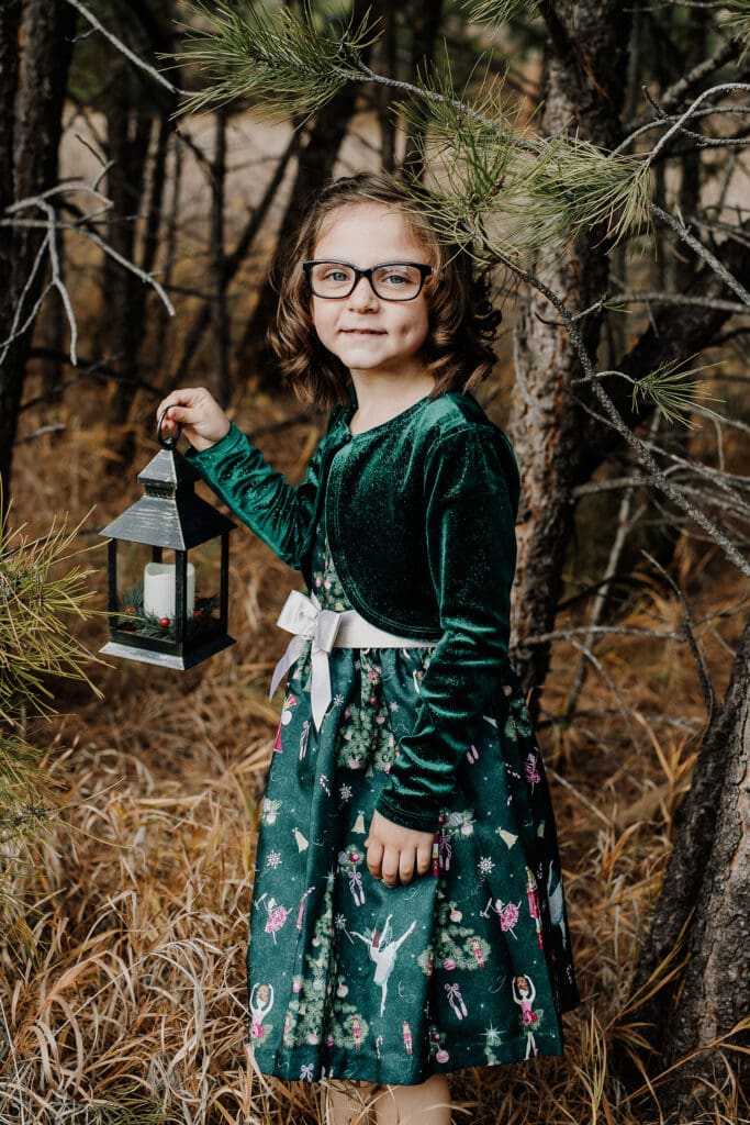 Girl in a Christmas dress in the woods holding a lantern in Rapid City, South Dakota